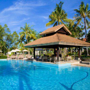 An image of a thatch hut in a coastal area next to a swimming pool. 