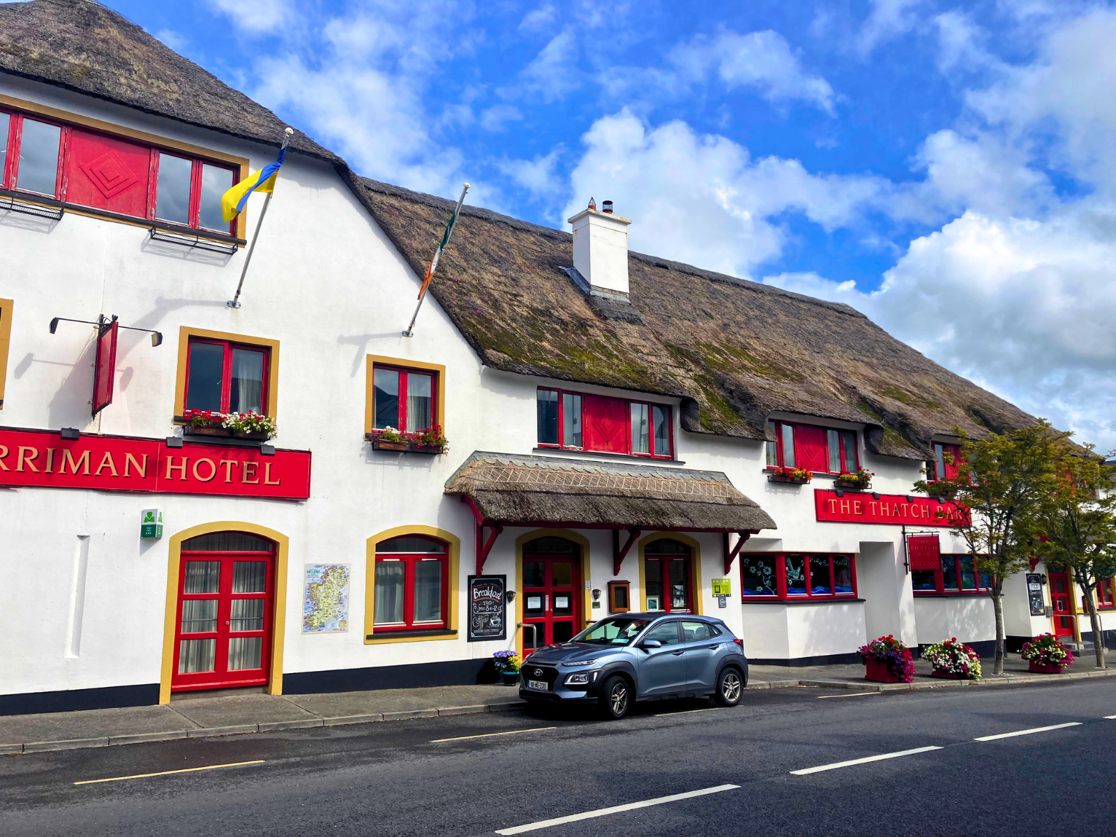 Full street view of the Marriman Hotel and The Thatch Bar, Ireland &mdash; a classic Irish thatched hospitality venue with white render, red signage, flower boxes, and a traditional reed roof &mdash; representing the commercial hospitality segment Endureed Somerset Premium is engineered to serve.