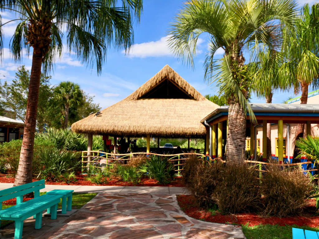 Endureed Premium Bali thatch pavilion at Chuy's restaurant, surrounded by palm trees, native Florida landscaping, and colorful teal benches along a stone pathway
