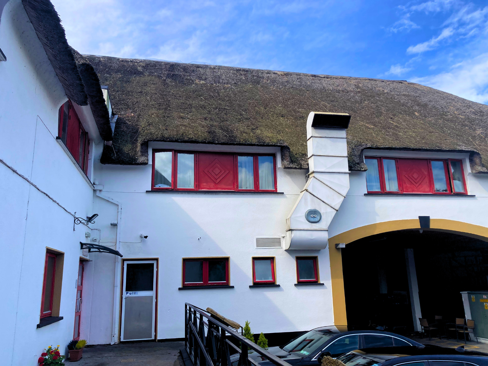 Full facade of the Thatch Bar featuring a wide traditional Irish thatched roof with red-framed dormer windows, white render walls, and a covered entrance &mdash; a commercial hospitality property showcasing the scale of a full thatch re-roof opportunity.