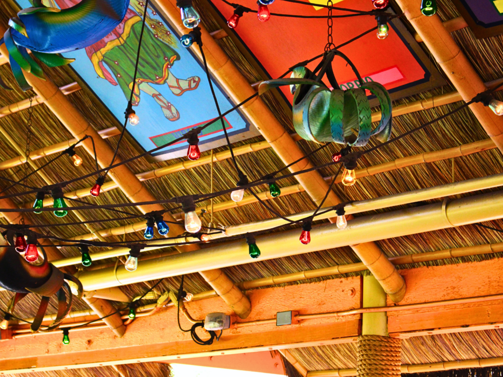 Interior view of an Endureed Premium Bali thatch and bamboo ceiling at Chuy's restaurant, featuring colorful string lights, decorative murals, and warm ambient lighting.