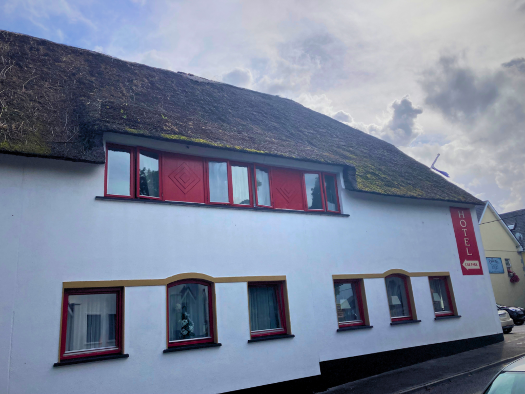 Street-facing facade of the Thatch Bar showing the full natural thatched roofline, red dormer windows, and arched ground-floor window details with gold render trim &mdash; a strong before reference for a Somerset Premium commercial rethatch project.