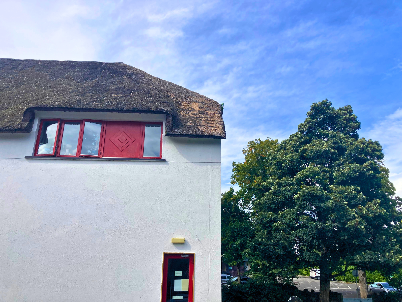 Side gable view of the Thatch Bar showing the hip-style thatched roof rising to a central peak, with red-framed windows and mature trees &mdash; demonstrating the architectural scale of a traditional Irish thatched commercial property.