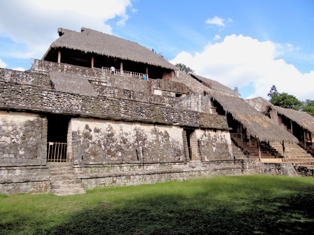 Wide hero view of Ek Balam Mayan acropolis in Yucatan Mexico featuring multiple levels of Endureed Performance Weathered Palm synthetic thatch roofing &mdash; engineered thatch protecting ancient stone terraces and stairways with visitors on upper platform