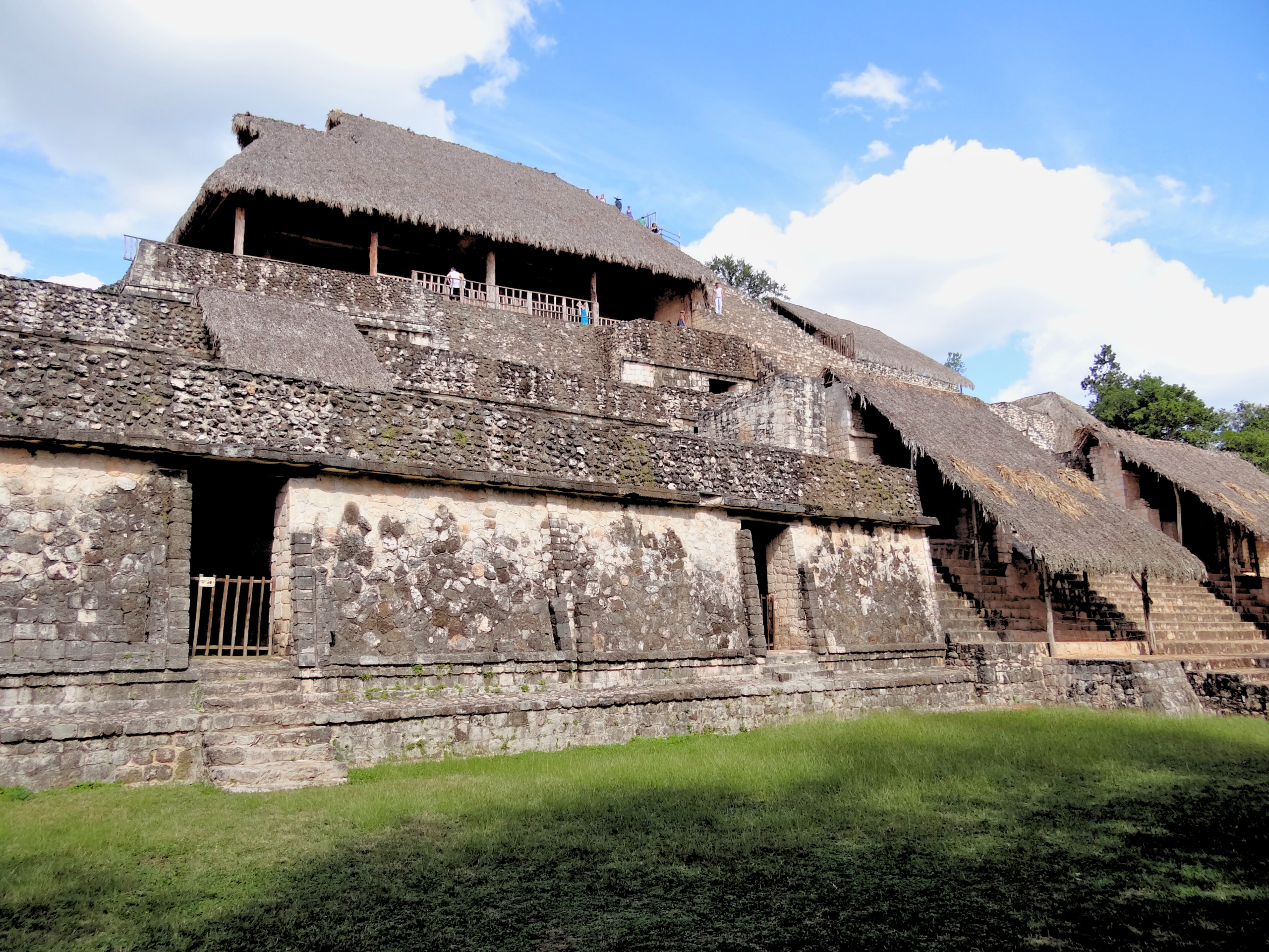 Wide hero view of Ek Balam Mayan acropolis in Yucatan Mexico featuring multiple levels of Endureed Performance Weathered Palm synthetic thatch roofing — engineered thatch protecting ancient stone terraces and stairways with visitors on upper platform