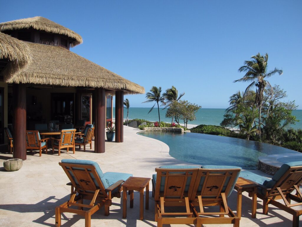 Baum residence on Sanibel Island, FL with Endureed Premium Bali synthetic thatch roof visible from the beach, palm trees blowing in the wind