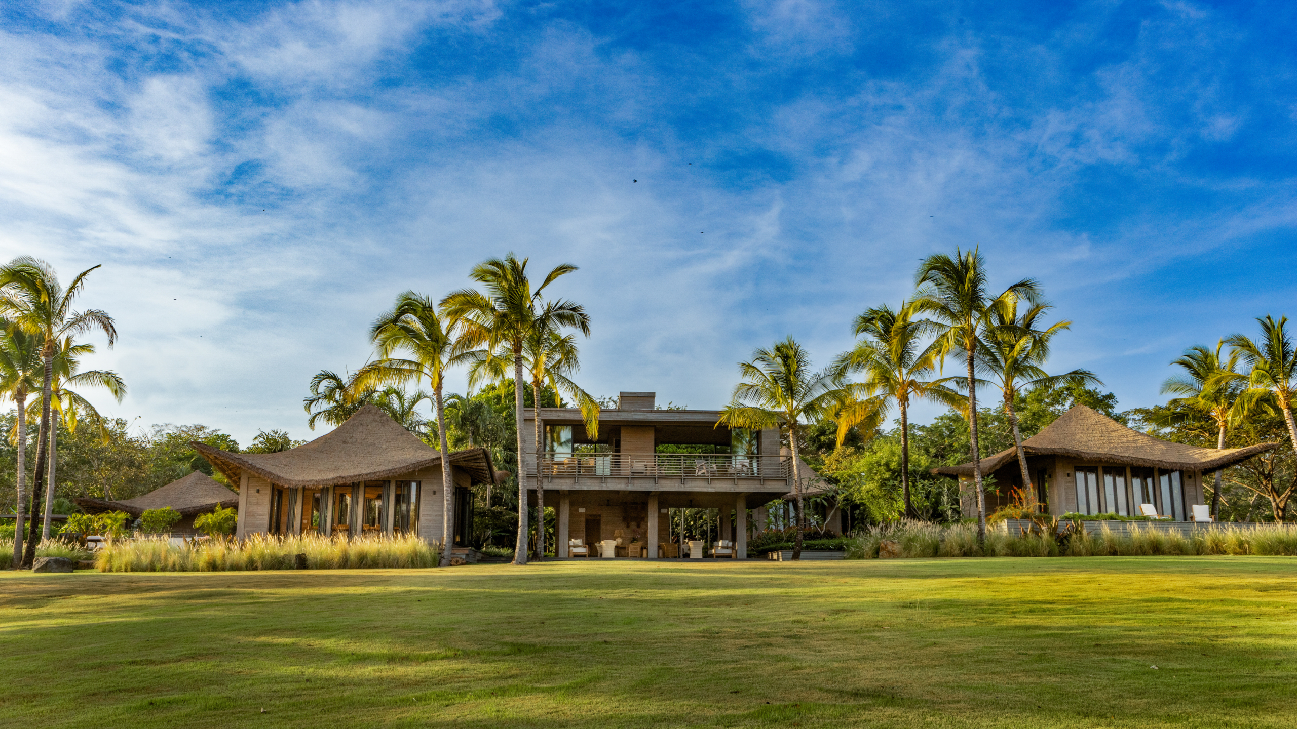 High-end modern tropical estate with dramatic sweeping thatched roofs and integrated pavilions.