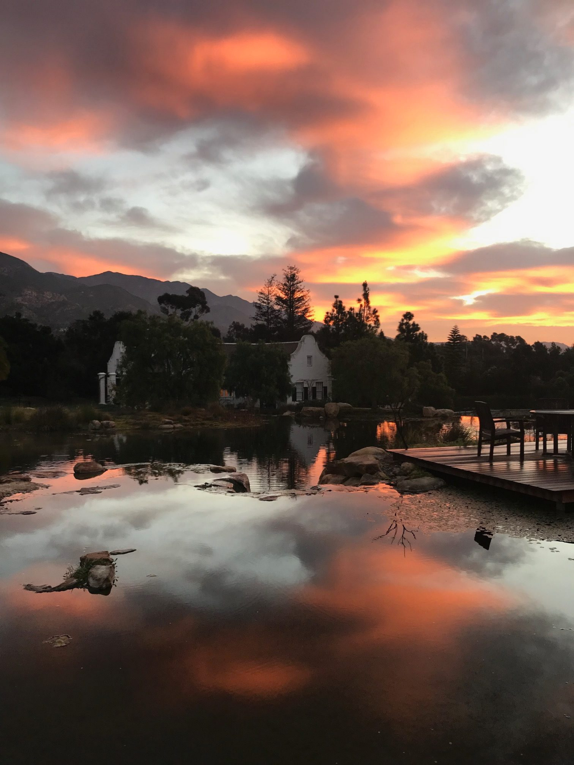 Endureed Premium Kilimanjaro synthetic thatch roof silhouette at Dean's Grange Malibu California &mdash; Cape Dutch luxury residence reflected in private lake at dramatic sunset with Santa Monica Mountains backdrop