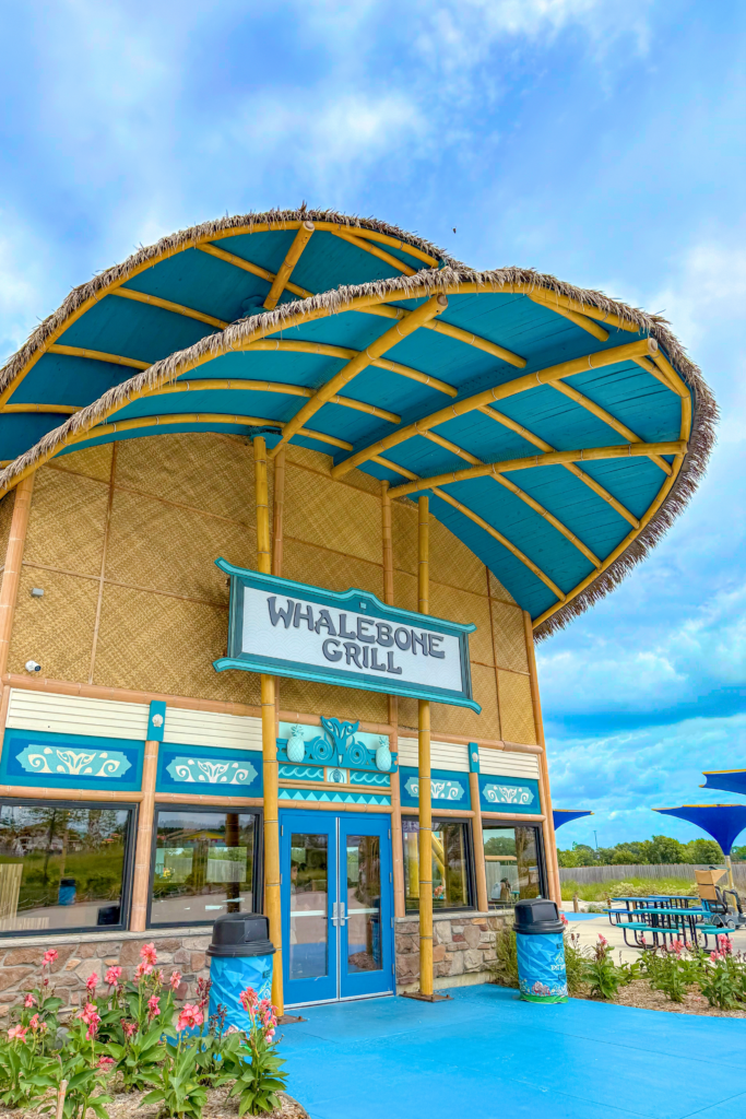 Endureed bespoke custom-colored synthetic thatch on Whalebone Grill restaurant canopy at Lost Island Theme Park Waterloo Iowa &mdash; engineered thatch fringe trim on large teal and bamboo shade structure over themed dining entrance