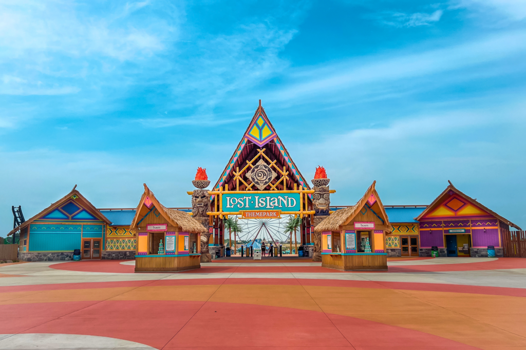 Lost Island Theme Park main entrance gate in Waterloo Iowa featuring Endureed Performance Palm synthetic thatch on ticket booth rooftops &mdash; engineered thatch on tribal-themed entry pavilions flanking colorful park gateway