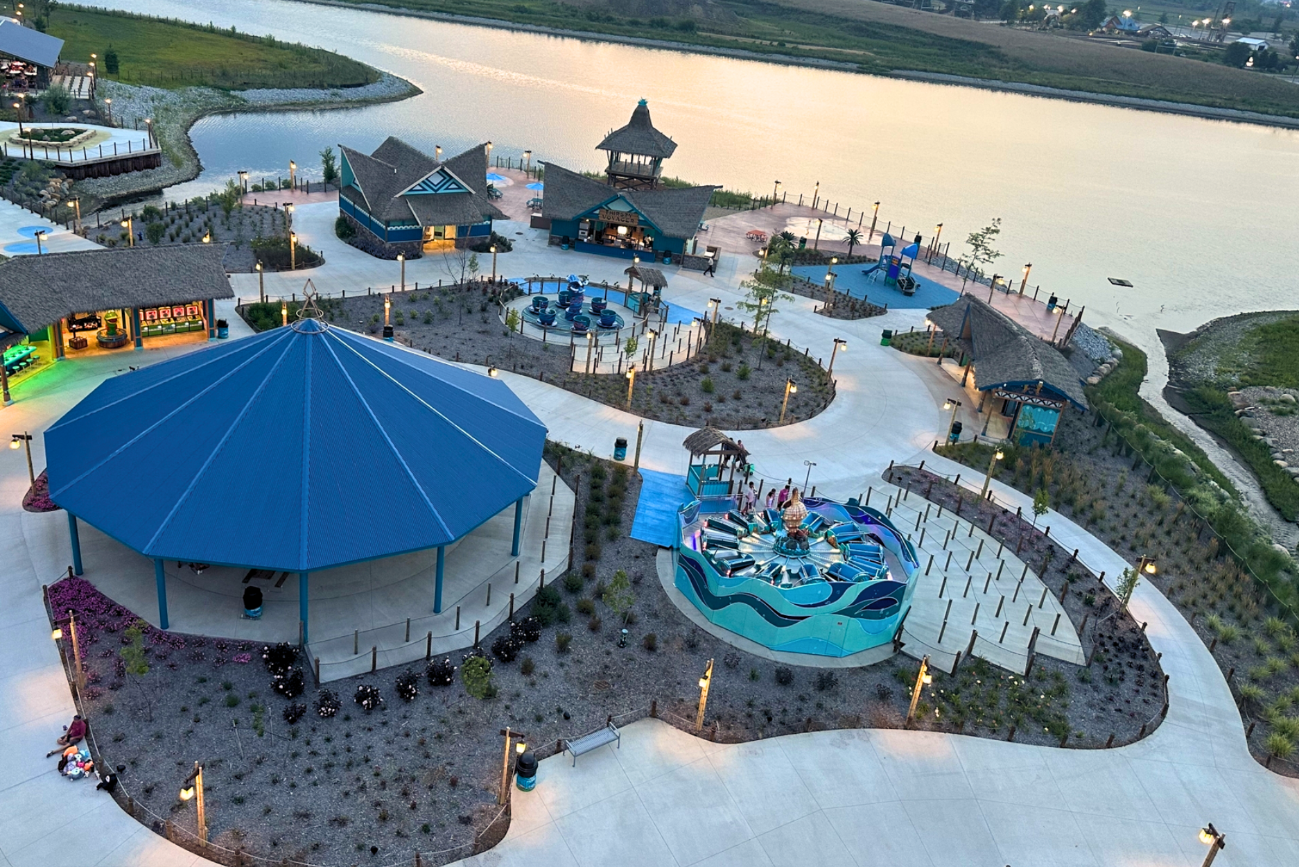 Aerial dusk view of Lost Island Theme Park Waterloo Iowa showing Endureed Performance Palm synthetic thatch on multiple structures throughout the park &mdash; engineered thatch rooftops visible across the waterfront themed zone at golden hour