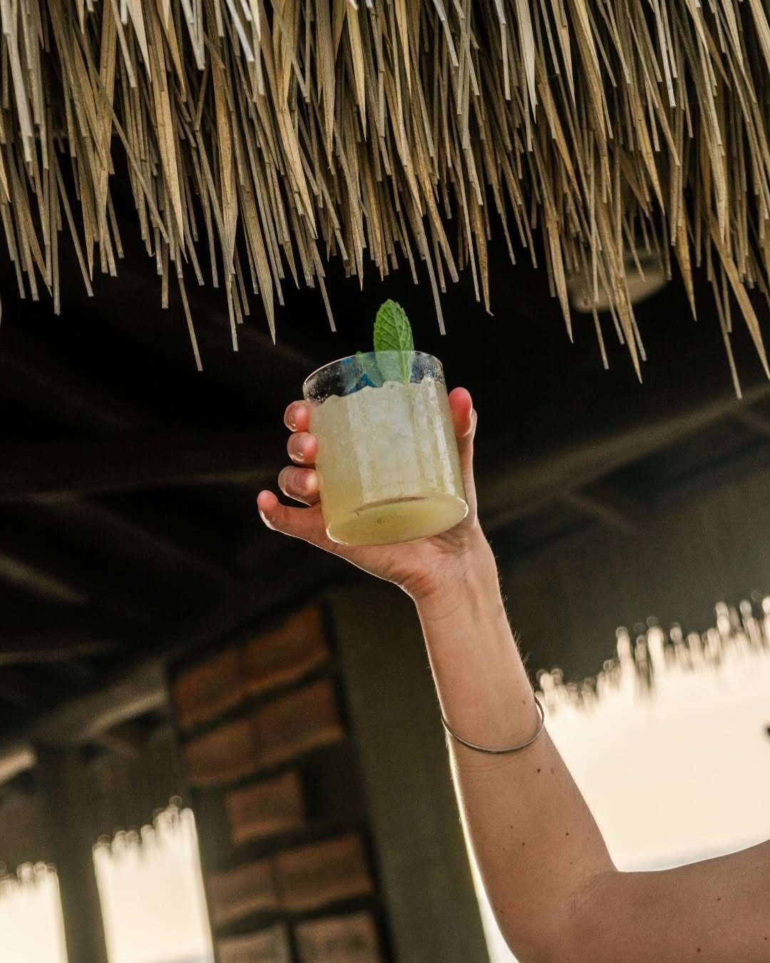 A garnished cocktail held beneath the thatch roofline at Kona Village