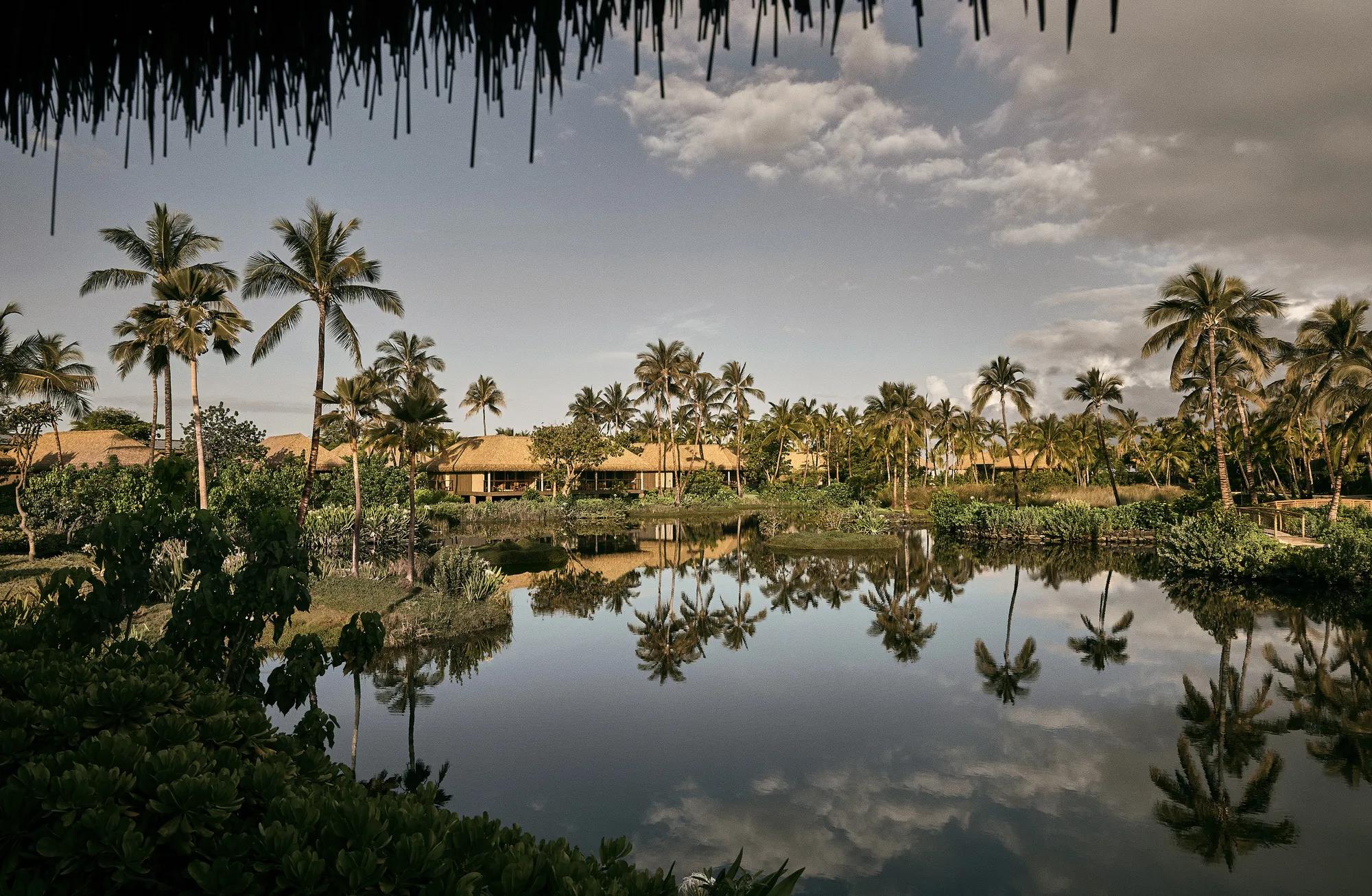 Thatched hale reflected in a lagoon at Kona Village at dusk