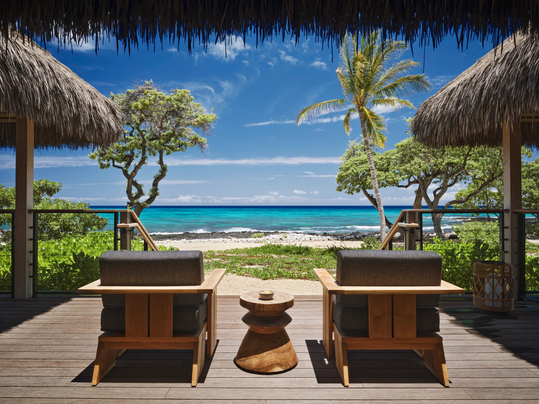 Ocean view from a Kona Village engineered thatch lanai, framed by palm trees and turquoise water