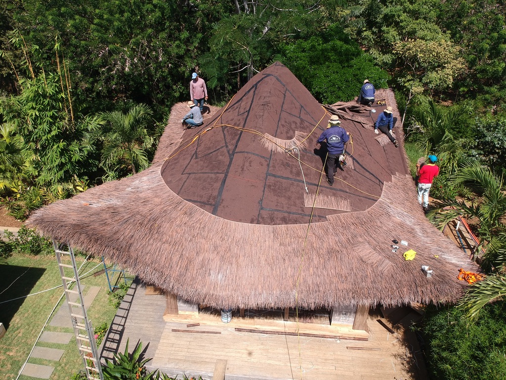 Aerial view of Casa Loro construction crew hand-installing engineered thatch roofing over underlayment on a pavilion roof in Pedasi, Panama