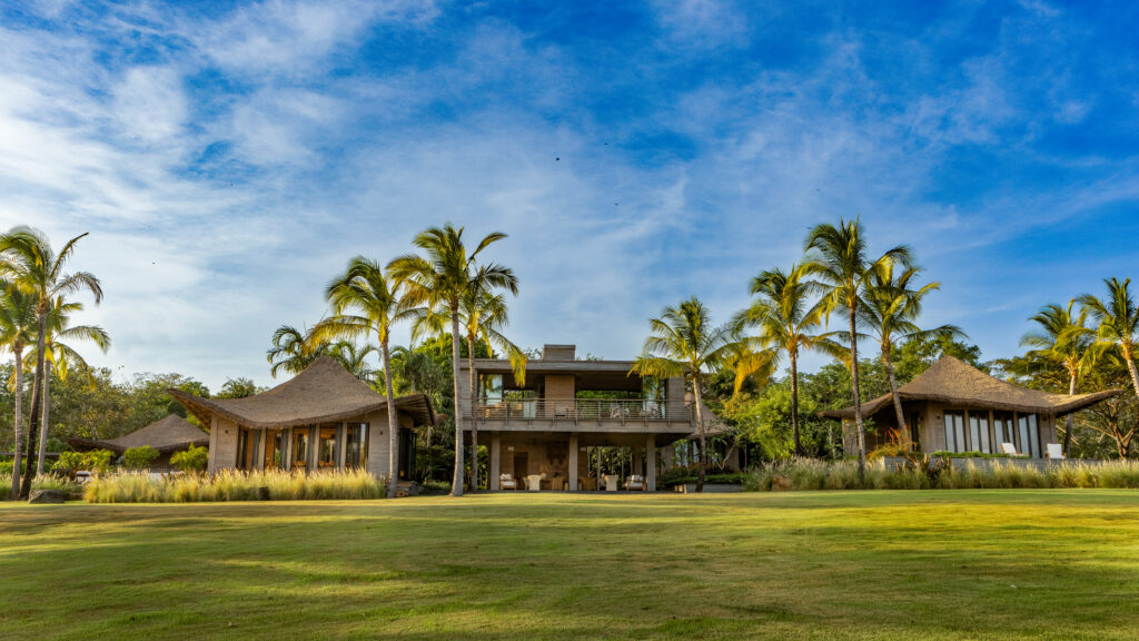 Casa Loro reveal, wide exterior view of the finished pavilions with Endureed engineered thatch roofing framed by royal palms on the Pacific coast in Pedasi, Panama, IM/KM Architecture